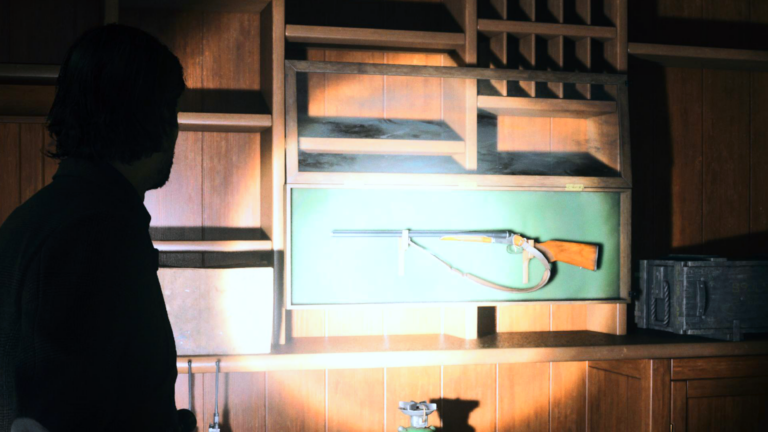 Alan steht in Alan Wake 2 vor einem Jagdgewehr, dass an einer Holzwand hängt.