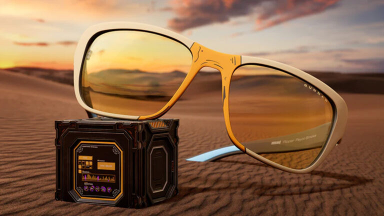 Eine gelbe Blaufilterbrille liegt im Sand auf einem Kästchen.