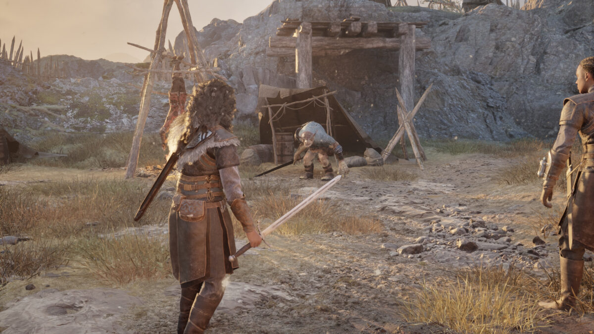 A woman with a sword faces an enemy near a wooden structure, with a companion standing beside her.
