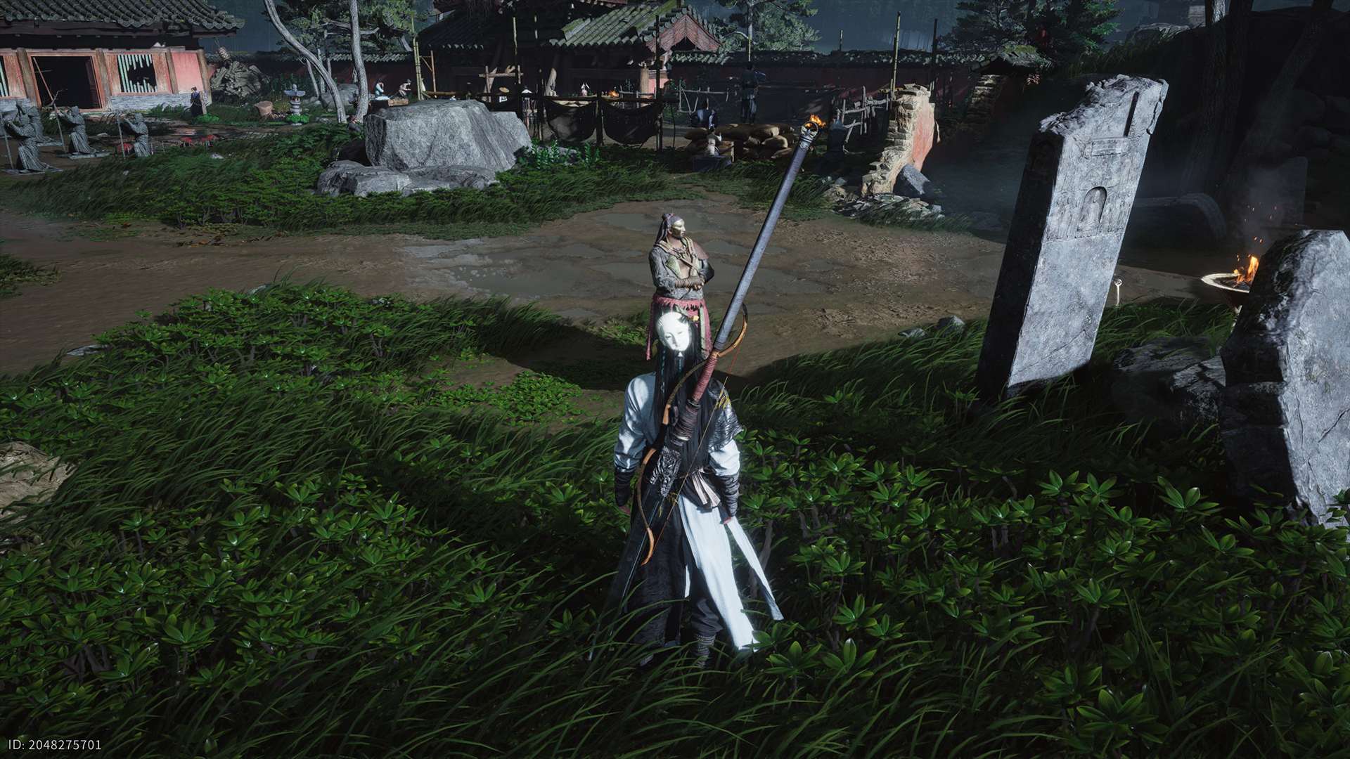 Ein maskierter Krieger mit langer Robe, Schwert und Speer steht im hohen Gras vor einer matschigen Arena. Hinter ihm lehnt eine Figur mit verschränkten Armen an einem Pfahl. Im Hintergrund sind Holzhütten, Übungsfiguren, Fackeln, Felsen und eine abgenutzte Steinstele zu sehen.