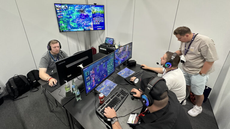 Eine Gruppe junger Männer, die an einem großen Schreibtisch an verschiedenen Monitoren auf der Gamescom spielen.