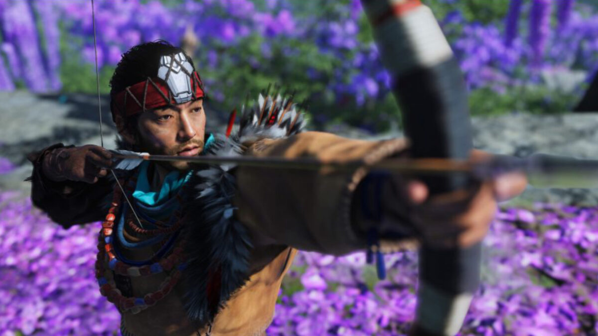 A man with a headband, bow and arrow standing in a flower field.