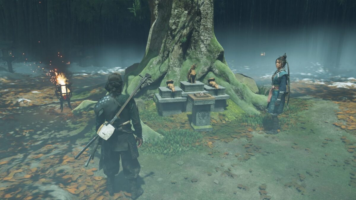 Atsu stands in a forest. In front of a tree are three statues on pedestals.