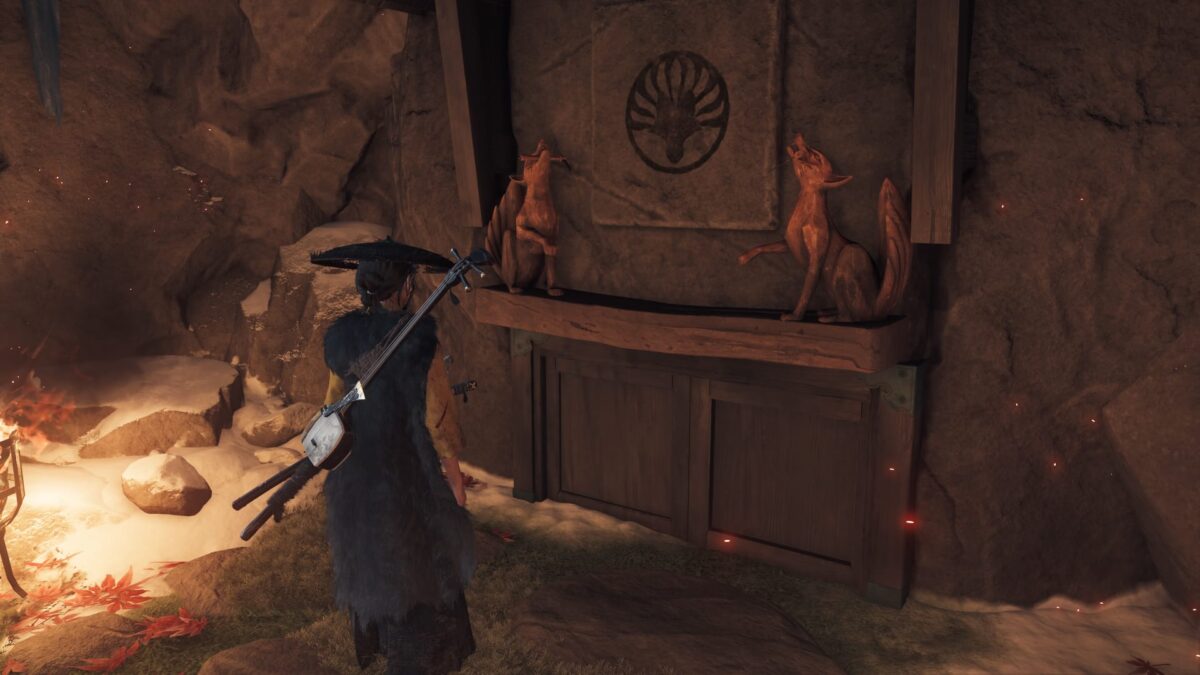 Zwei Fuchsstatuen aus Holz auf einem Balken. Mittig davon ein Symbol.