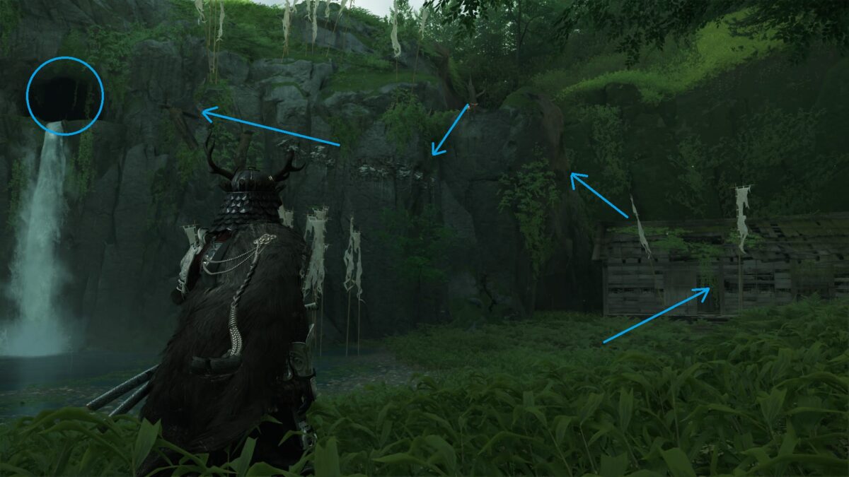Atsu steht vor einer Felswand, rechts ein zerfallenes Haus, links oben eine Höhle.