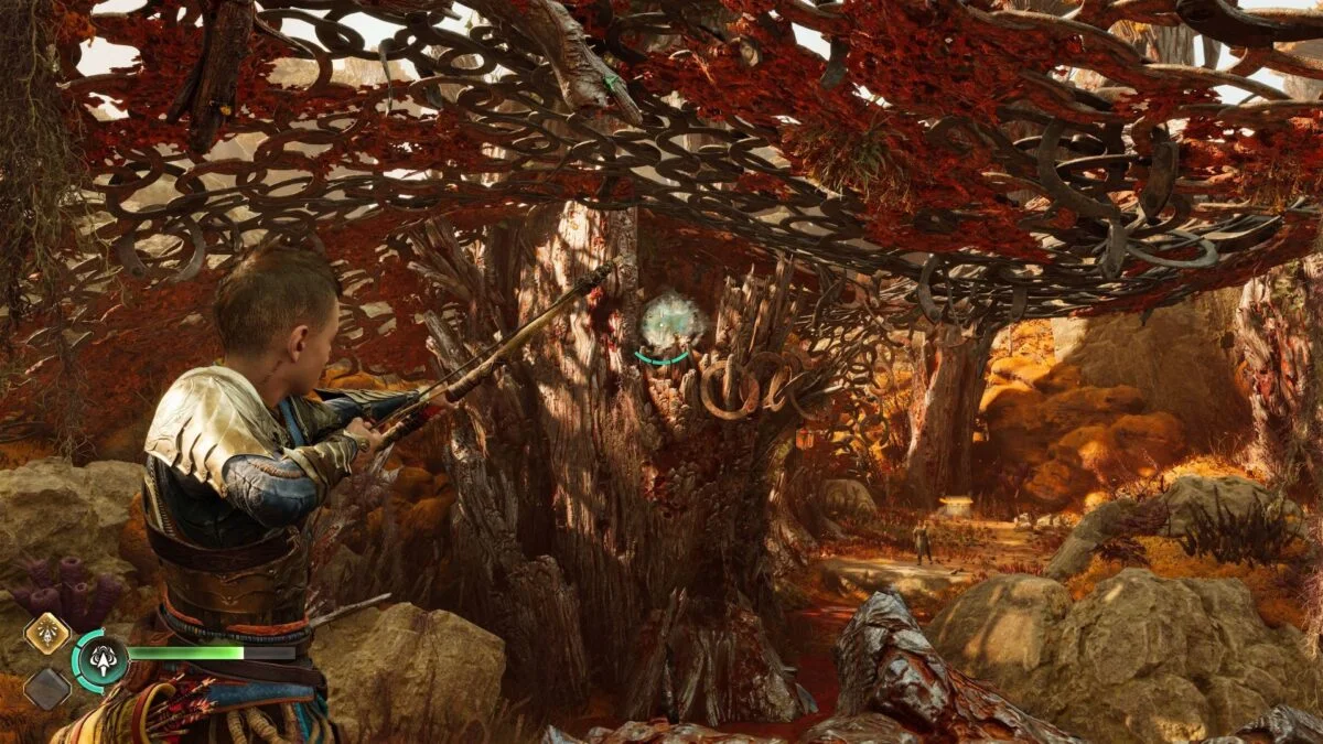 Atreus zielt in God of War Ragnarök mit dem Bogen auf einen grün schimmernden Klingstein, der an einem Baum befestigt ist. 