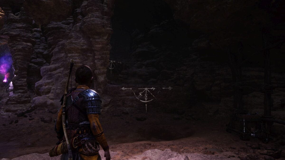 Atreus steht in God of War Ragnarök in einer dunklen Höhle vor einer Felswand mit weißten Markierungen.