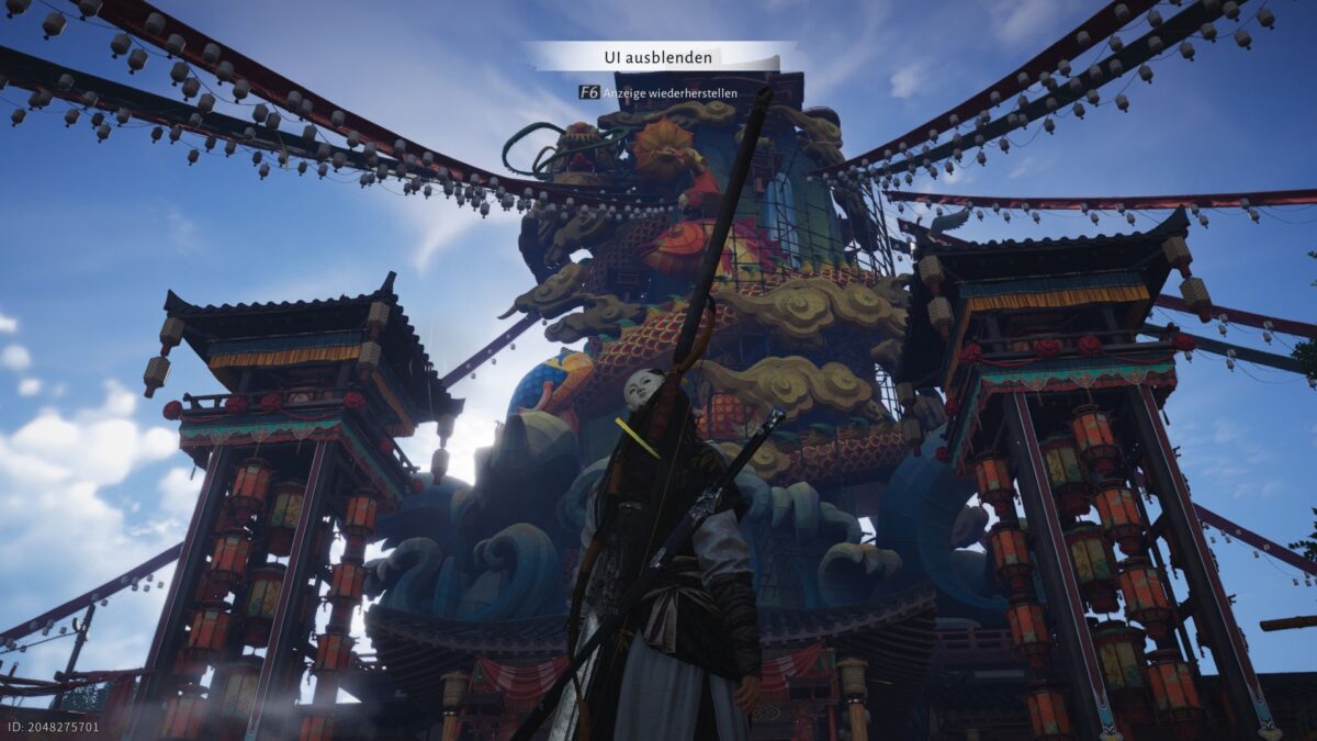 Spielfigur in traditioneller Rüstung steht vor einer riesigen, bunt verzierten asiatischen Tempel- und Festtagskonstruktion mit Drachen- und Wolkenmotiven, flankiert von hohen Laternentürmen und überspannt von langen Girlanden aus Laternen, unter einem klaren blauen Himmel.