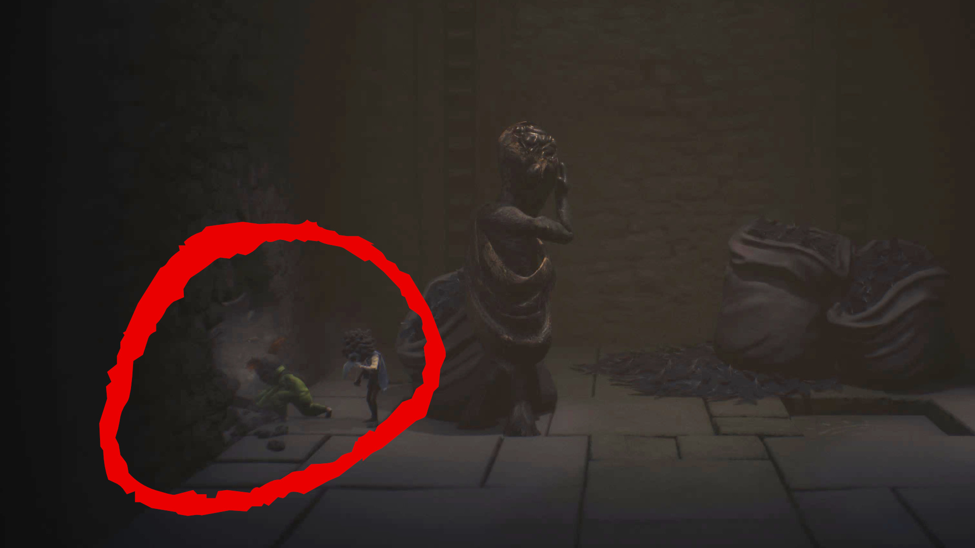 Zwei maskierte Kinder wundern sich in Little Nightmares 3 über einen Riss in der Wand in einem dunklen Raum mit einer großen Statue.