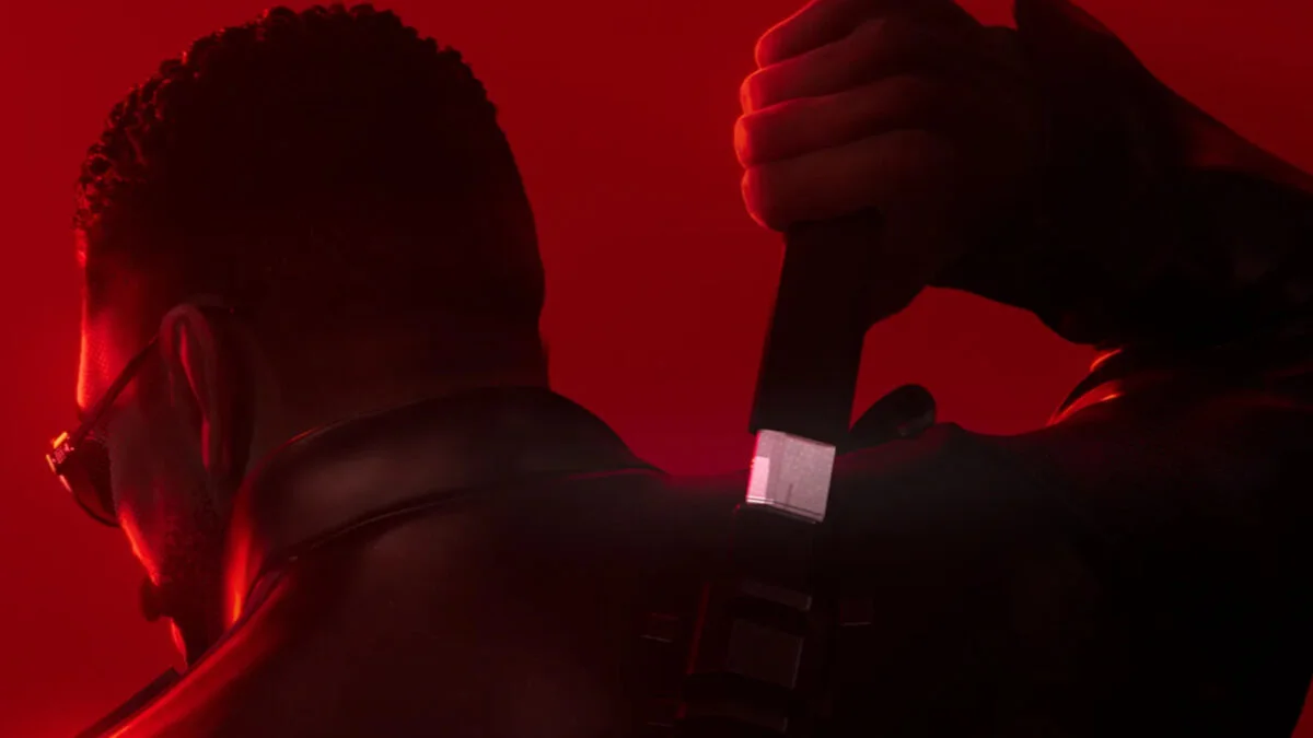 Ein Mann mit Sonnenbrille zieht vor einem roten Hintergrund ein Schwert aus der Halterung an seinem Rücken.