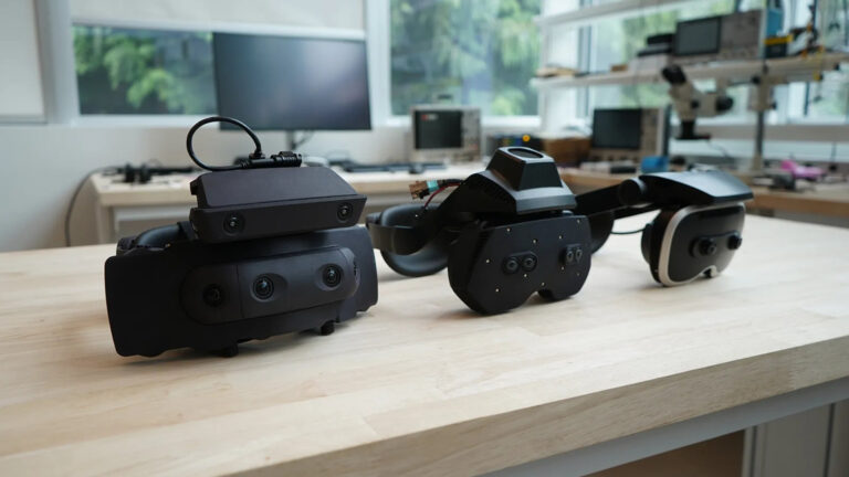 Drei schwarze VR-Brillen-Prototypen von Meta auf einem Holztisch.