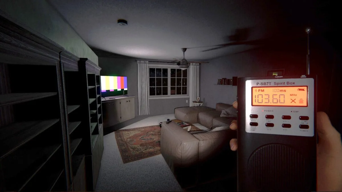 Jemand steht mit einer Geisterbox in der Hand in einem Wohnzimmer, während der Fernseher läuft.