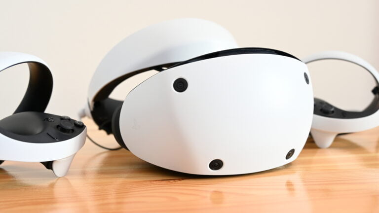 VR-Brille Playstation VR 2 auf einem Tisch von halblinks, mit Sense Controllern rechts und links