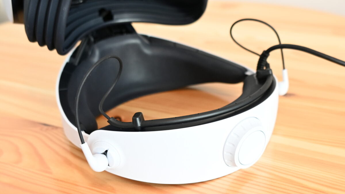 Die In-Ear-Ohrhörer der Playstation VR 2 direkt am hinteren Halobereich der VR-Brille, die umgedreht auf einem Tisch liegt