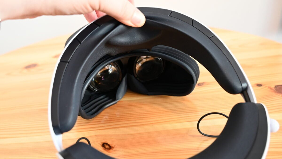 Hand drückt mit Dauemn auf Stirnplster von PSVR 2, die VR-Brille liegt auf einem Tisch