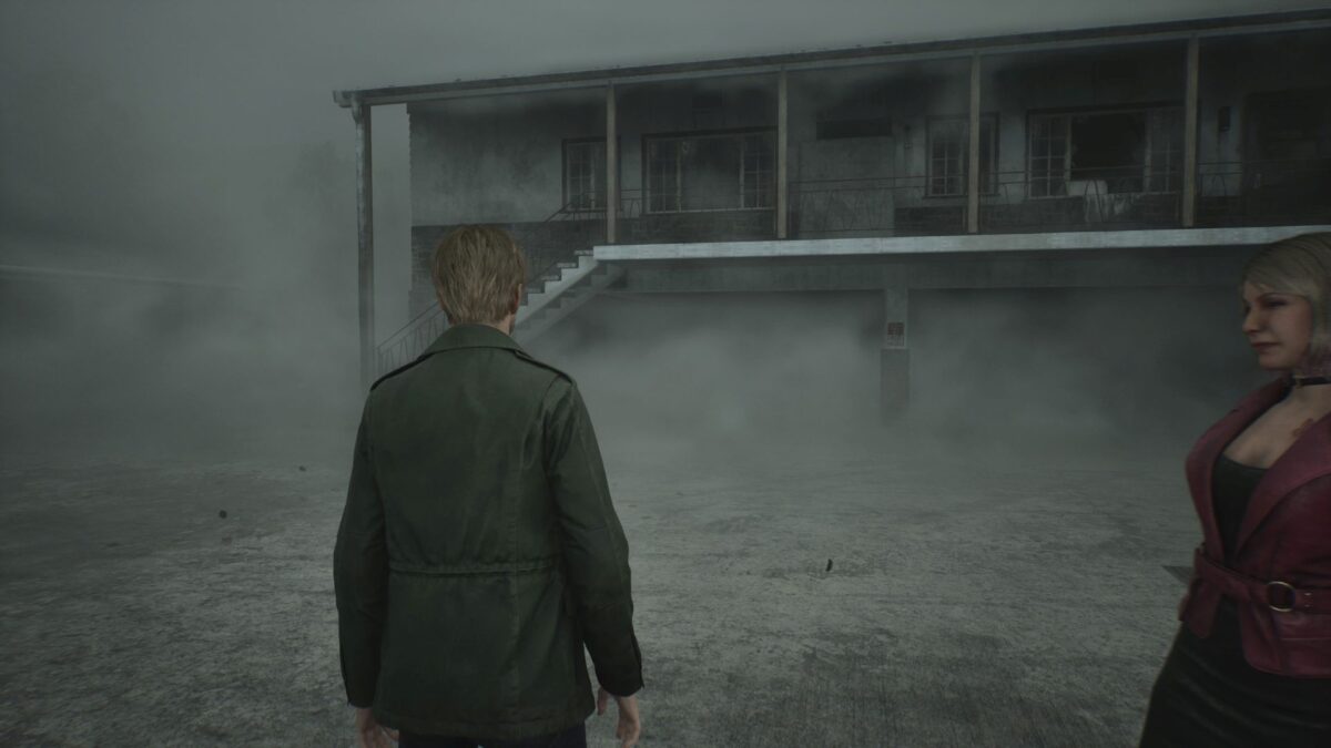 James steht in Silent Hill 2 in einer Motel-Anlage und blickt auf ein eingeschlagenes Fenster.