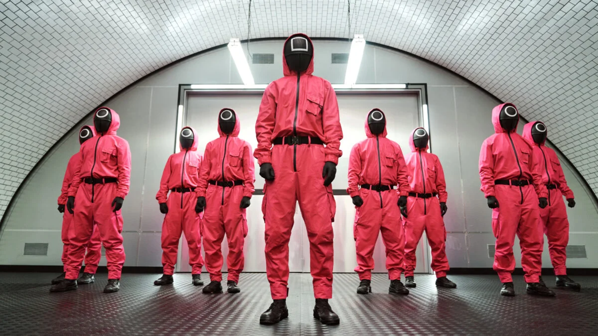 Mehrere maskierte Personen in pinken Ganzkörperanzügen aus der Netflix-Serie Squid Game.