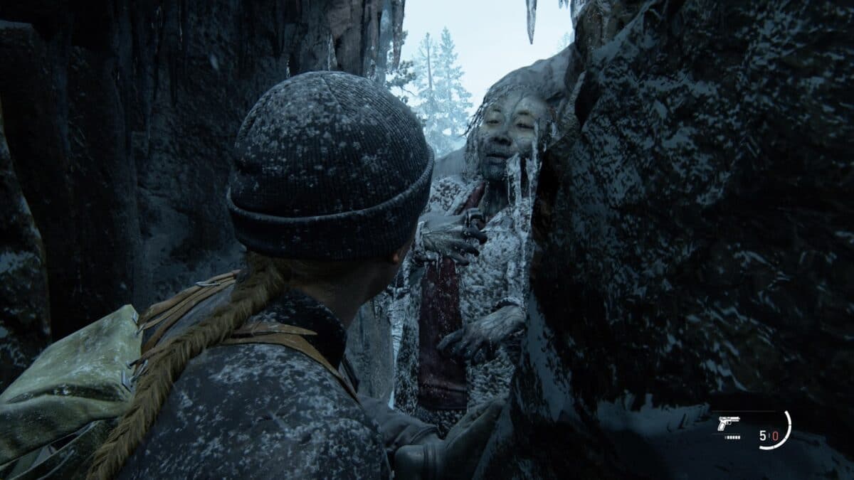 Eine Frau mit Mütze drückt sich durch eine Felsspalte, an deren Ende die gefrorene Leiche einer anderen Frau eingeklemmt ist.