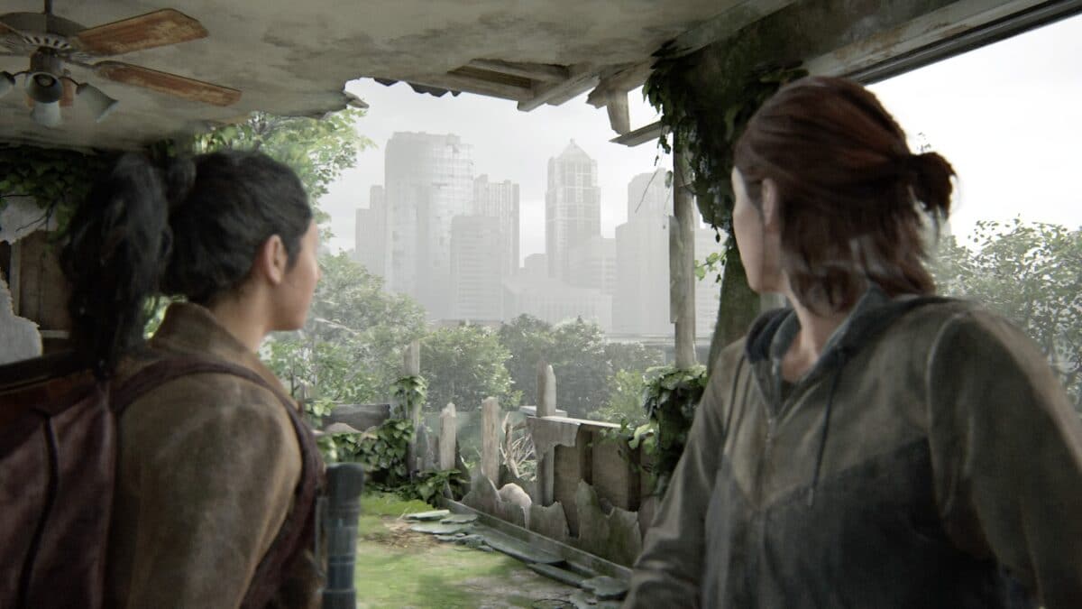 Dina und Ellie blicken durch eine zerstörte Wand auf ein paar Hochhäuser in der Ferne.
