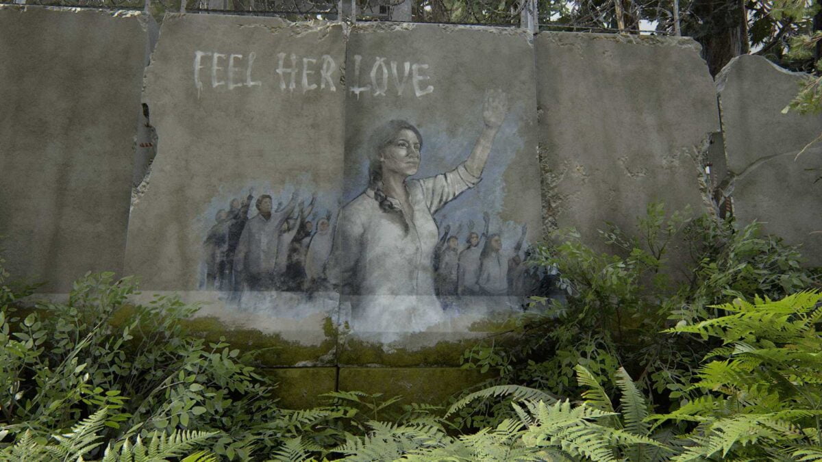 Ein Graffiti an einer rissigen Wand in The Last of Us Part 2 zeigt eine Frau mit erhobenem Arm. Im Hintergrund sieht man viele Menschen mit der gleichen Geste. Darüber steht "Feel her Love" in weißen Buchstaben. 