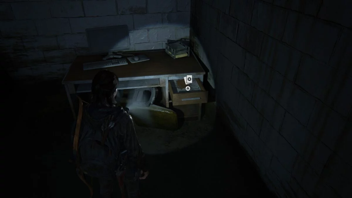 Ellie steht in The Last of Us 2 vor einem Schreibtisch, in dessen Schublade eine Sammelkarte liegt.