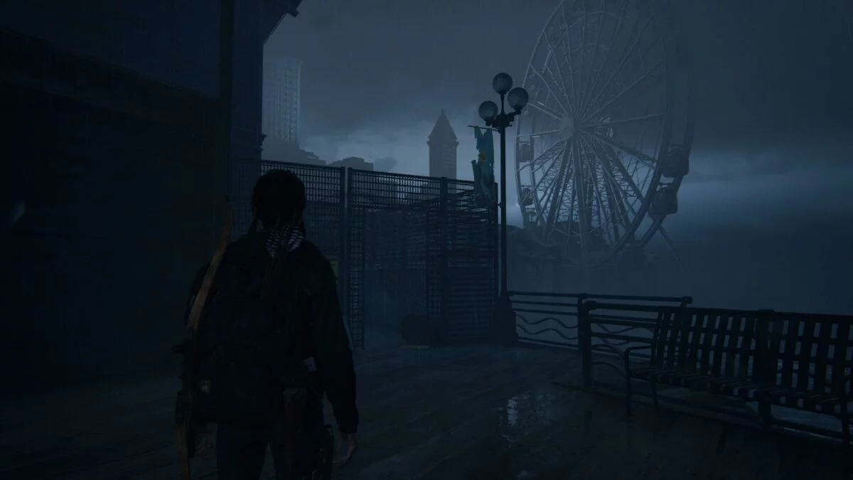 Ellie steht in The Last of Us 2 vor einem kaputten Zaun mit Blickrichtung auf ein Riesenrad.