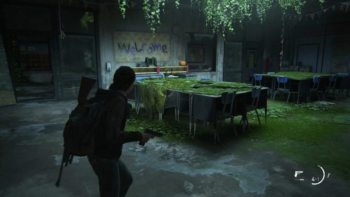 Ellie mit Waffe in einem Klassenzimmer der Eastbrook-Grundschule in The Last of Us 2