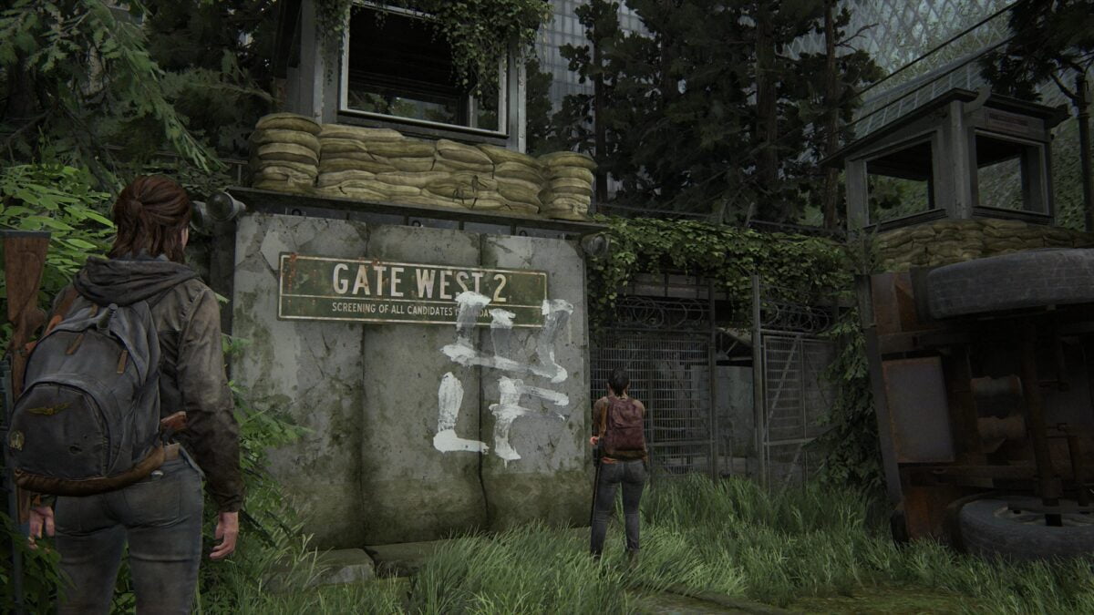 Ellie und Dina vor dem mit WLF-Graffitti beschmierten und befestigten Gate West 2 in Seattle in The Last of Us 2