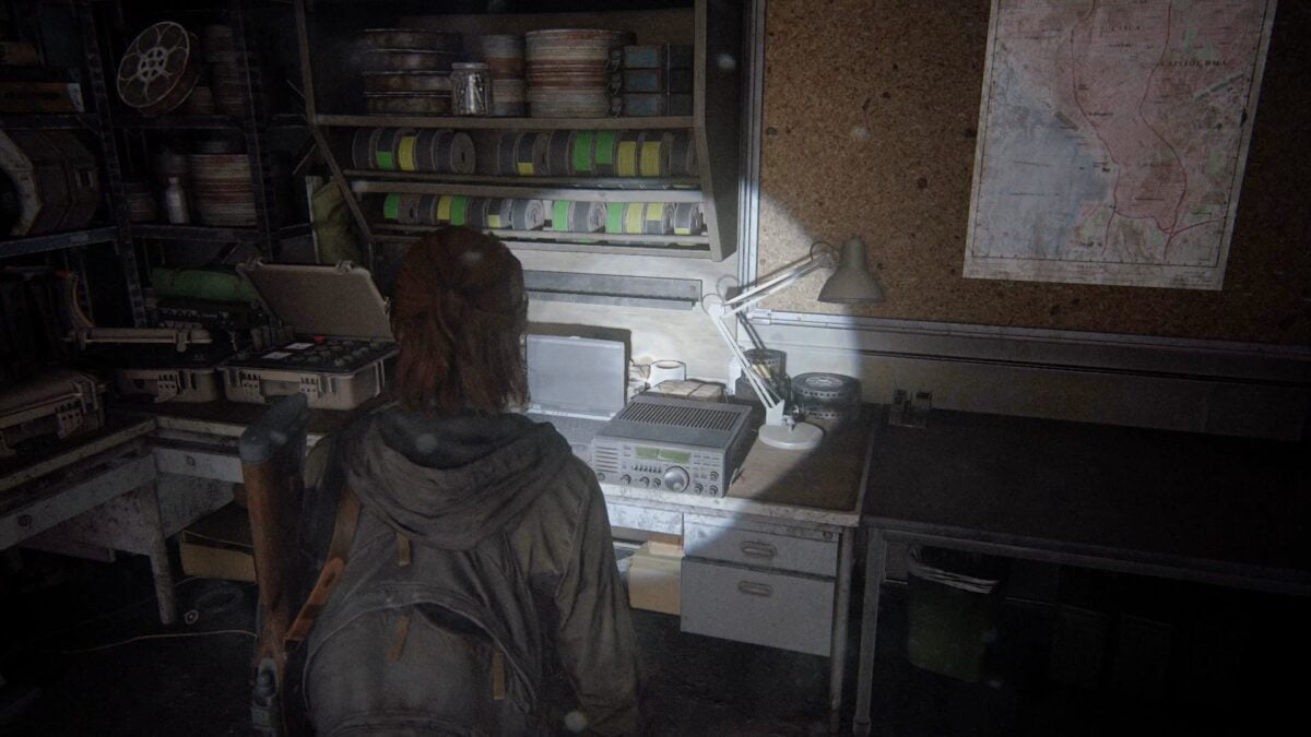 Ellie steht in The Last of Us Part 2 vor einem alten Funkgerät, das auf einem Tisch steht.