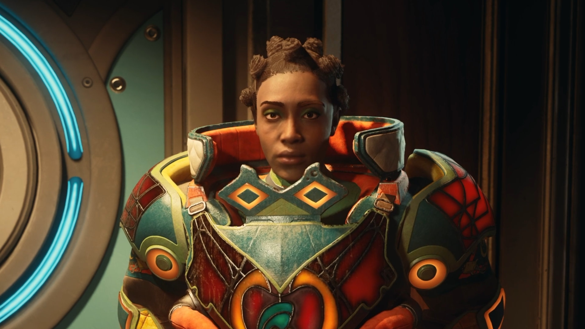A woman in silver and orange armor looks seriously into the camera, standing in a dimly lit metallic room illuminated by neon lights.