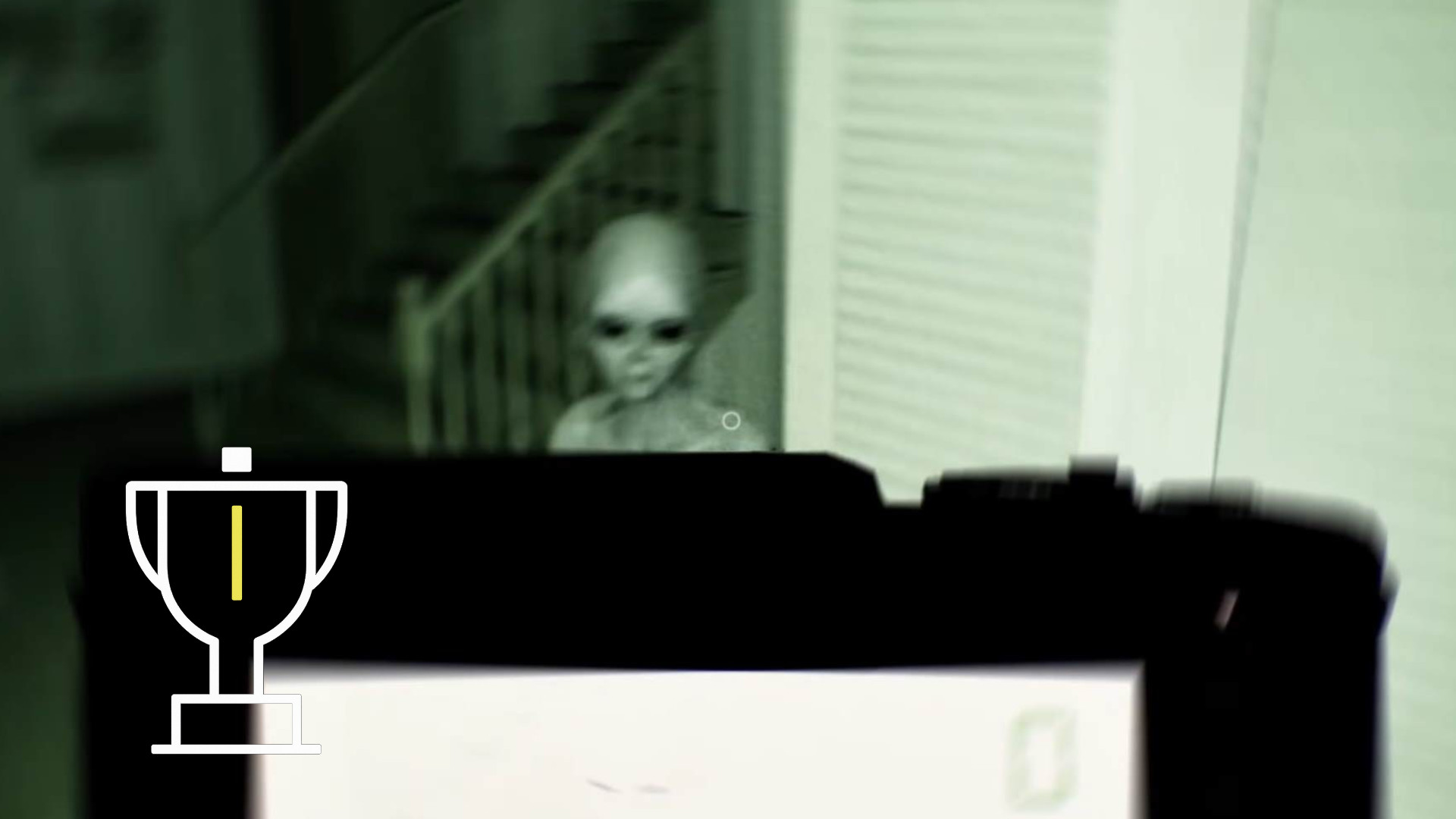 An alien stands in front of a staircase while a person points a camera at him.