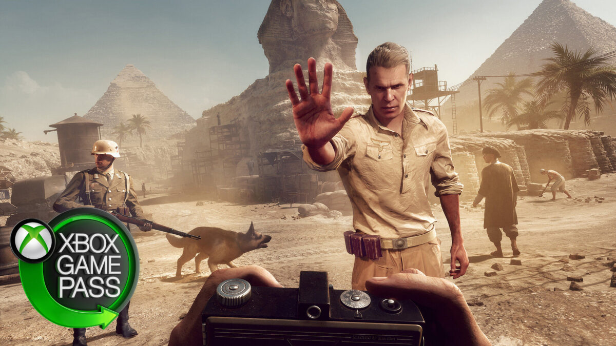 A man stands in the middle of the desert with his hand raised.