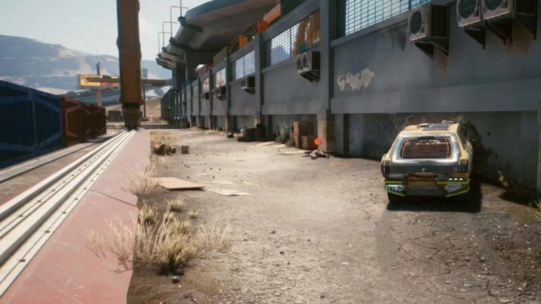 Cyberpunk 2077 Kleidung-Guide Leiche liegt vor Industriegebäude in einer Gasse hinter Containern, kaputtes Auto im Vordergrund