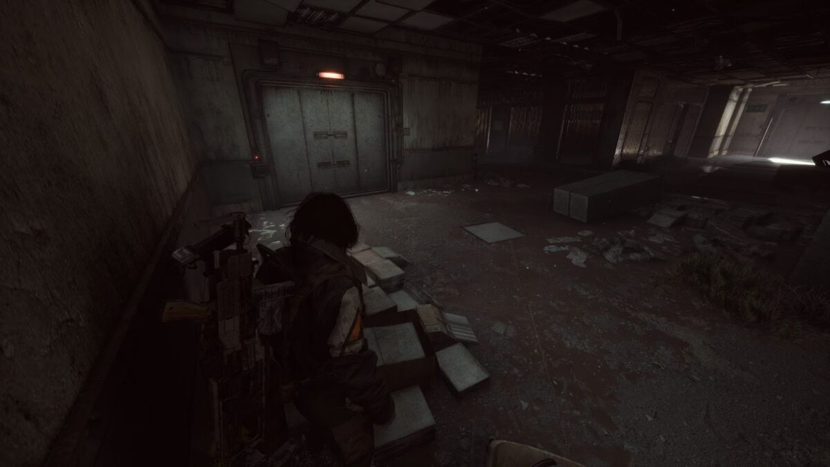 Dunkler, heruntergekommener Innenraum mit verschlossener Stahltür und rotem Warnlicht; der Charakter steht zwischen Schutt, zerbrochenen Fliesen und alten Metallkisten.