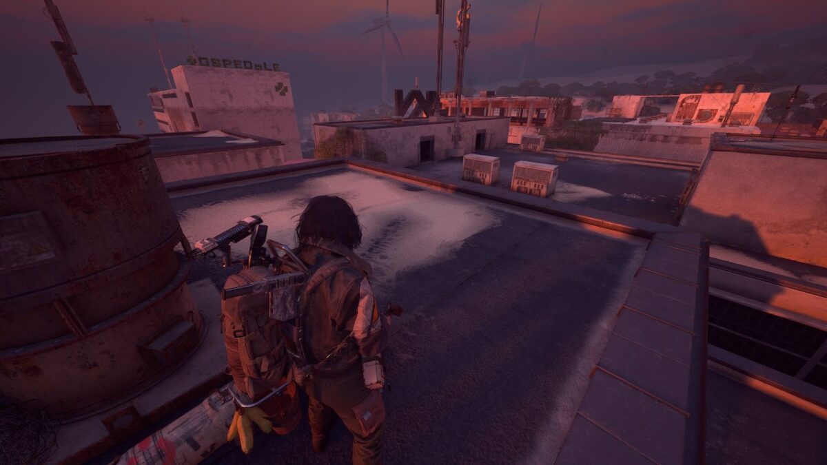 Postapokalyptische Rooftop-Szene im Abendlicht, in der ein ausgerüsteter Charakter über die Dächer der Begrabenen Stadt blickt; im Hintergrund verlassene Gebäude, Windräder und ein verblasstes „Ospedale“-Schild.